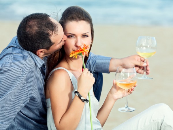 Young beautiful couple drinking wine on the beach